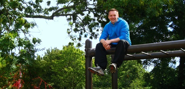 Muddy Plimsolls co-founder Jason Doggett seated on top of monkey bars